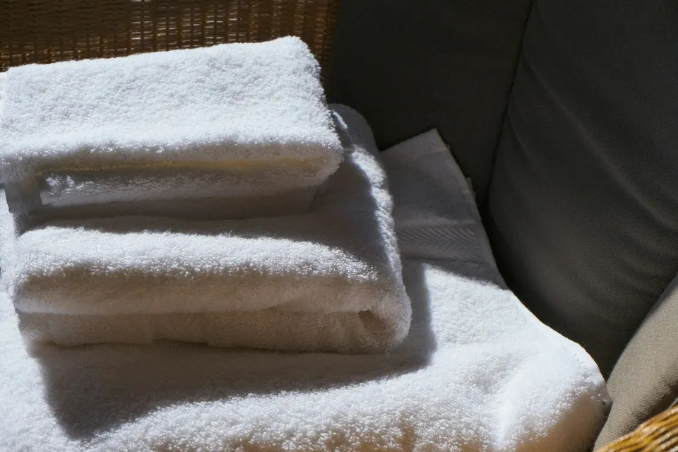 Clean white bath towels stacked on a wicker chair in natural light